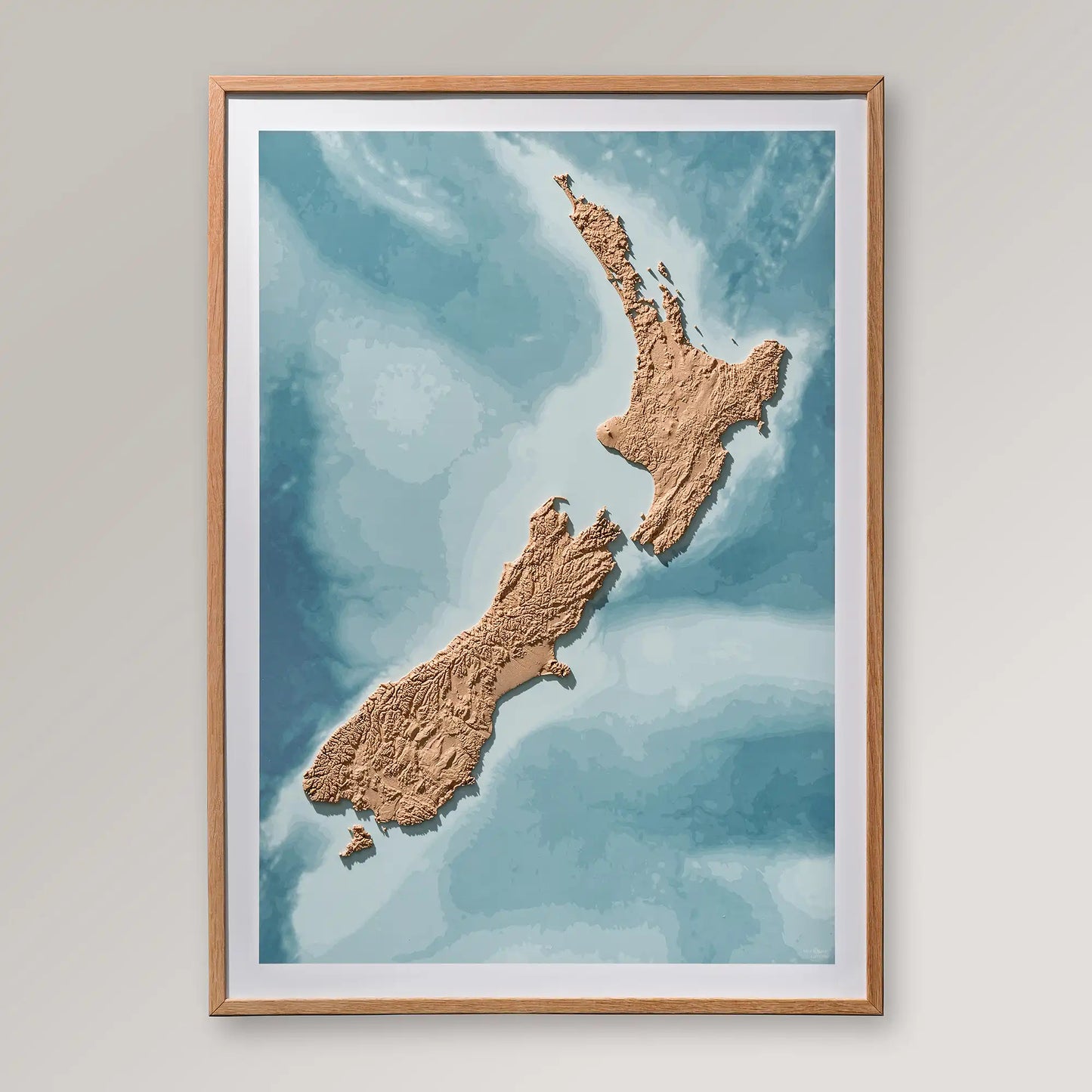 Framed 3D topographic map of New Zealand inside an oak frame on a light grey wall – TerraFrames