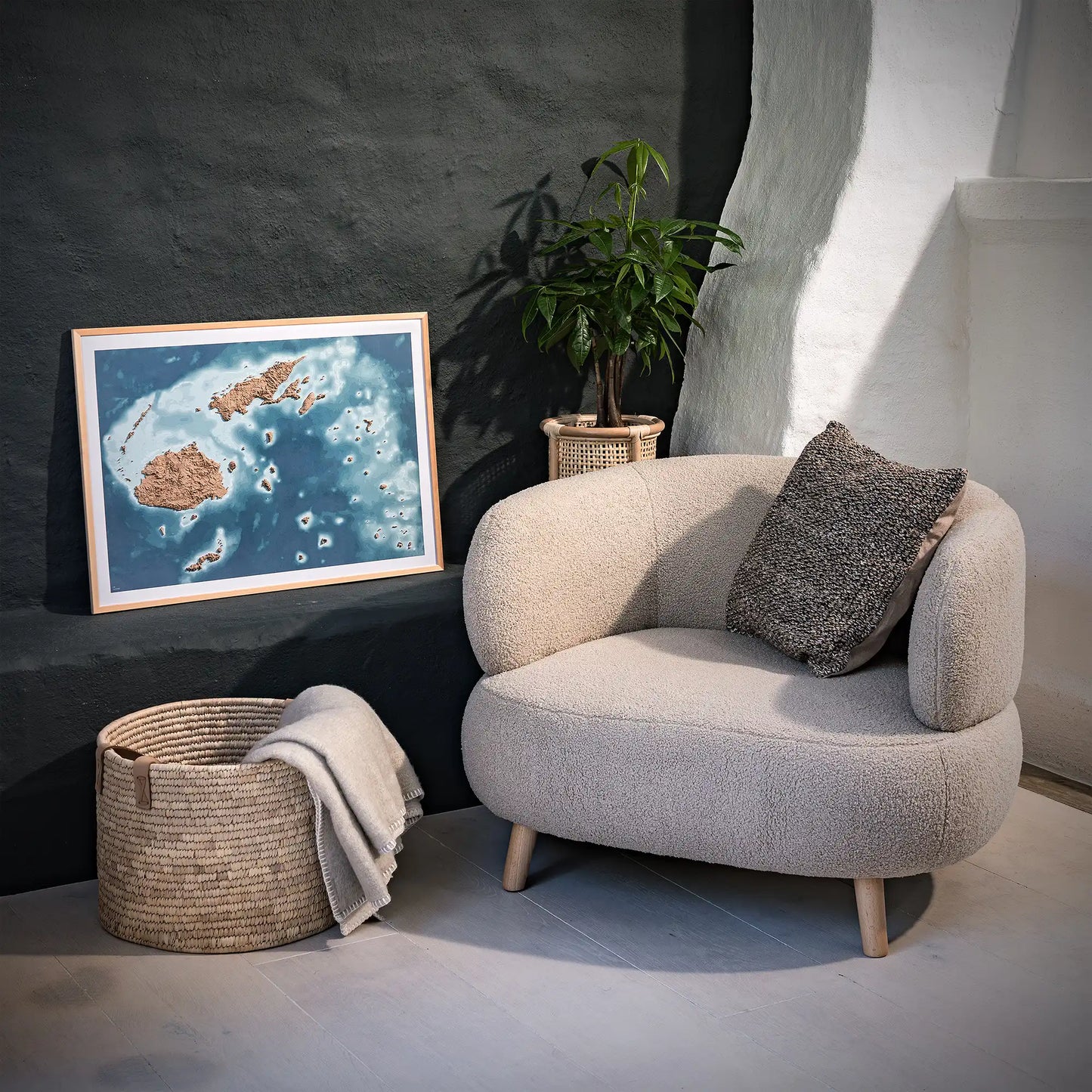 Framed 3D topographic map of Fiji, in a minimalist room with a beige armchair, a woven basket, a plant and a black wall – TerraFrames