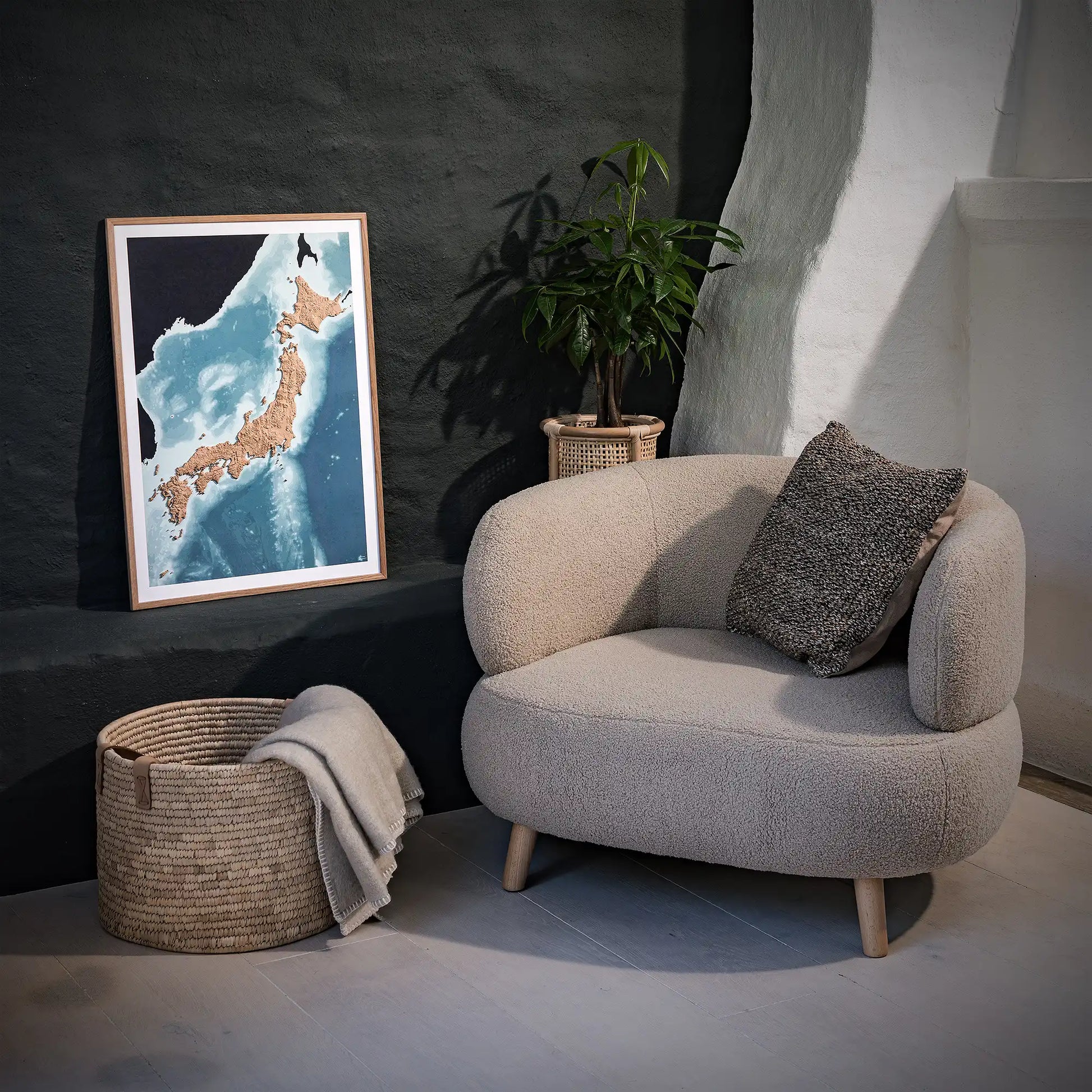 Framed 3D topographic map of Japan, in a minimalist room with a beige armchair, a woven basket, a plant and a black wall – TerraFrames