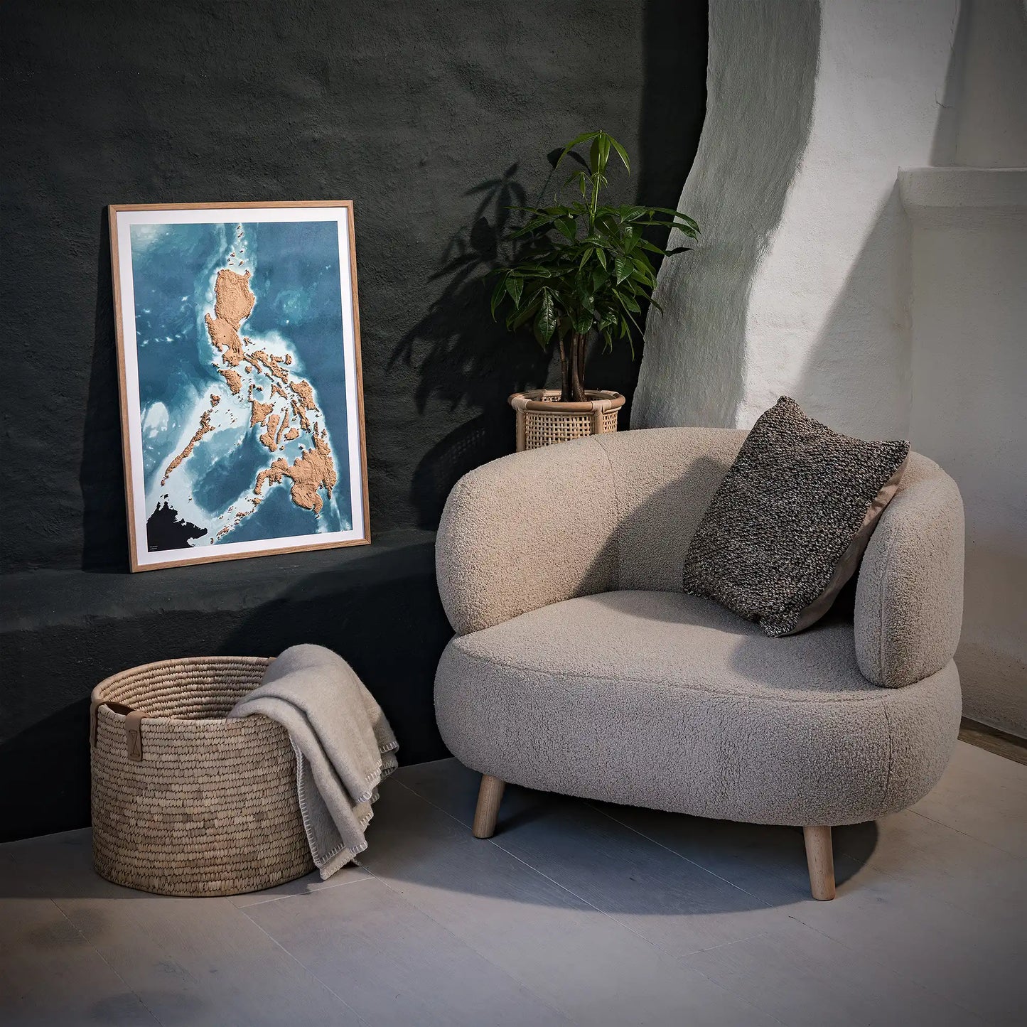 Framed 3D topographic map of the Philippines, in a minimalist room with a beige armchair, a woven basket and a black wall – TerraFrames