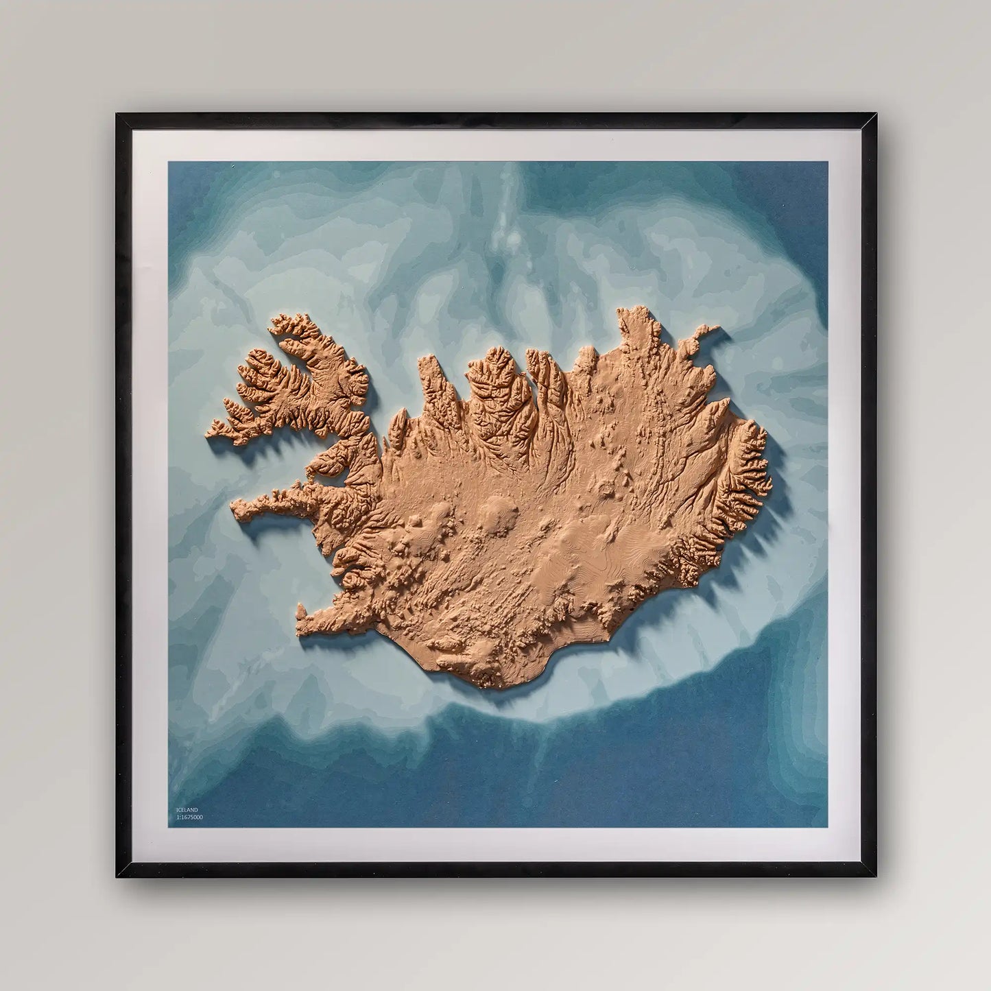 Framed 3D topographic map of Iceland, 40x40cm art board inside a black frame on a light grey wall – TerraFrames