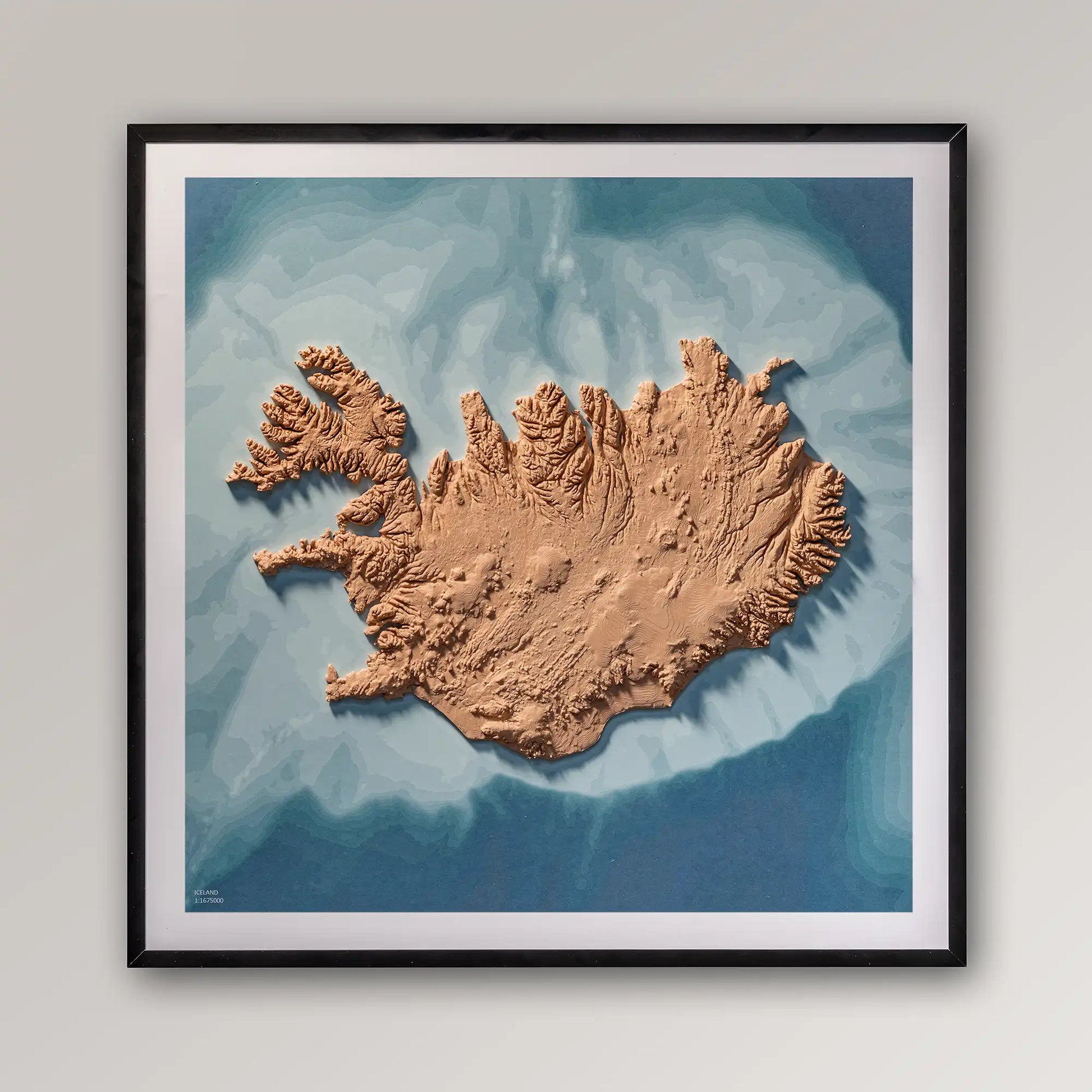 Framed 3D topographic map of Iceland, 40x40cm art board inside a black frame on a light grey wall – TerraFrames