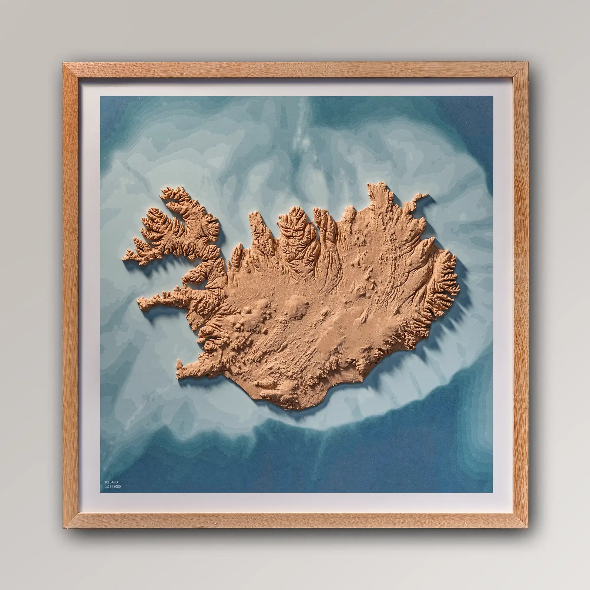 Framed 3D topographic map of Iceland, 40x40cm art board inside an oak frame on a light grey wall – TerraFrames