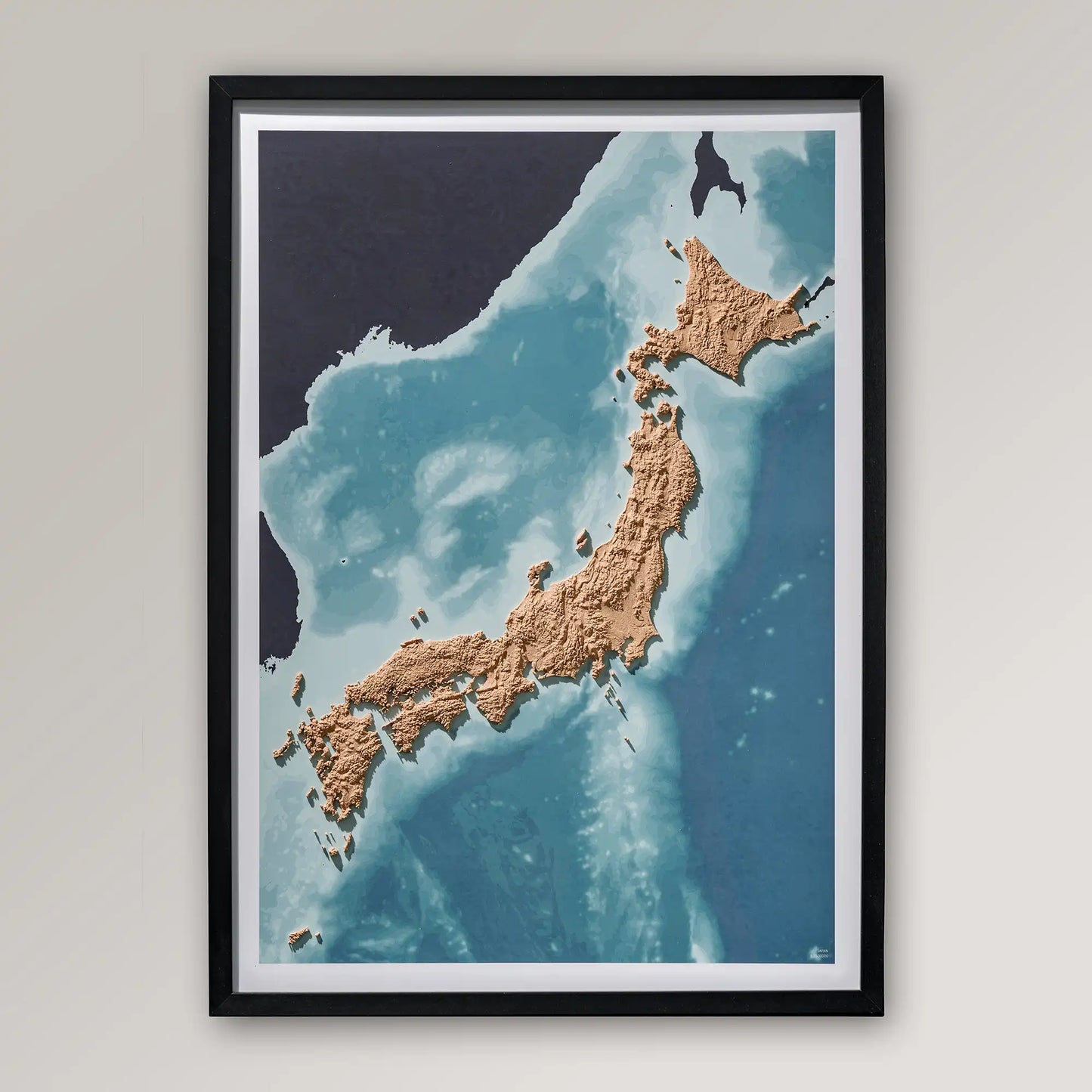Framed 3D topographic map of Japan inside a black frame on a light grey wall – TerraFrames