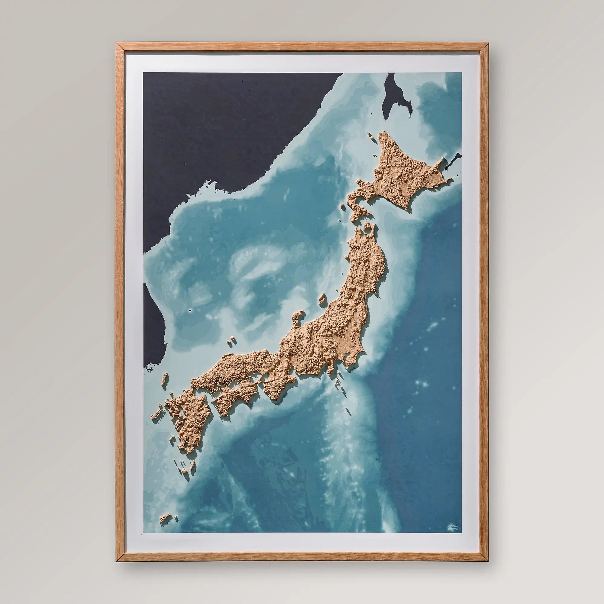 Framed 3D topographic map of Japan inside an oak frame on a light grey wall – TerraFrames