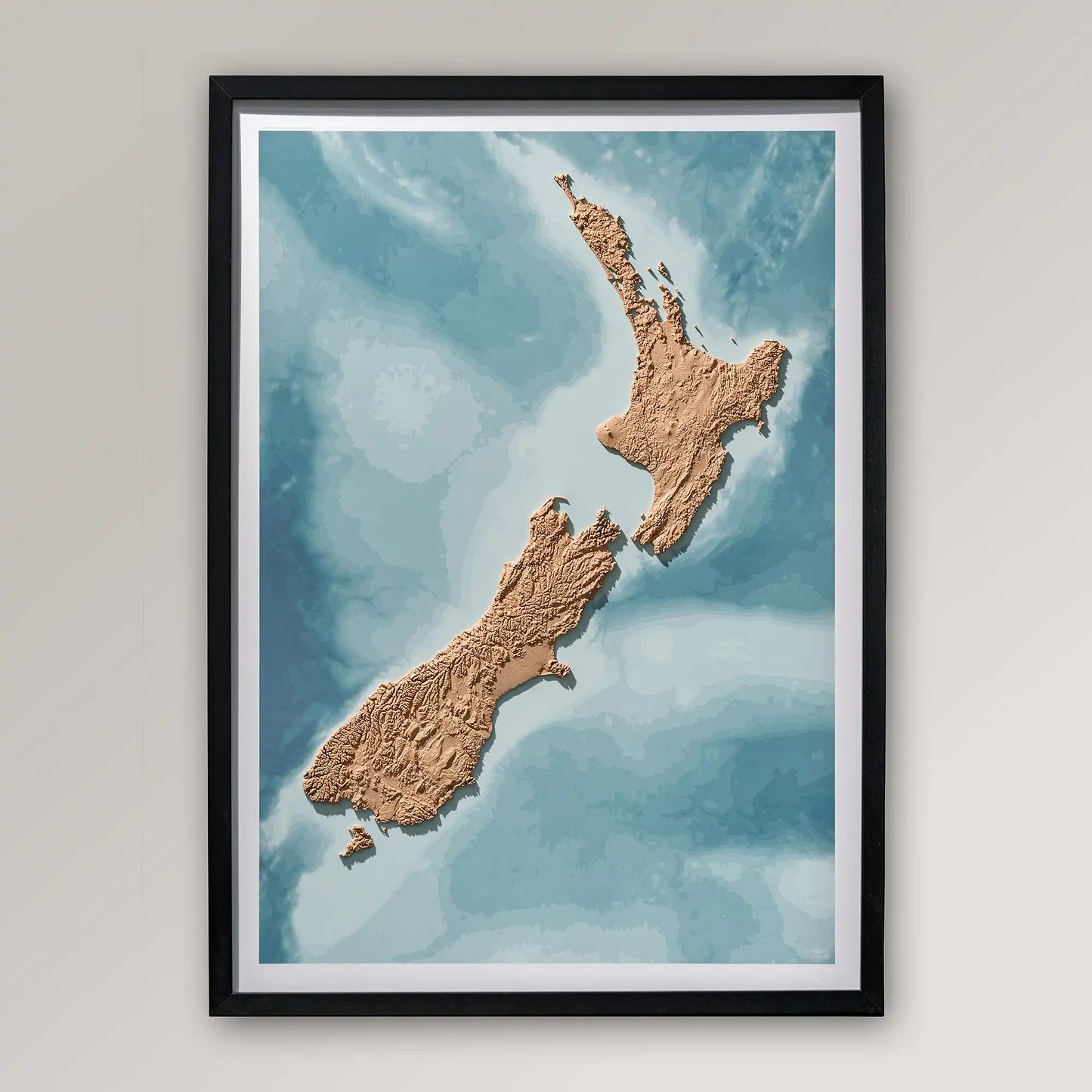 Framed 3D topographic map of New Zealand inside a black frame on a light grey wall – TerraFrames