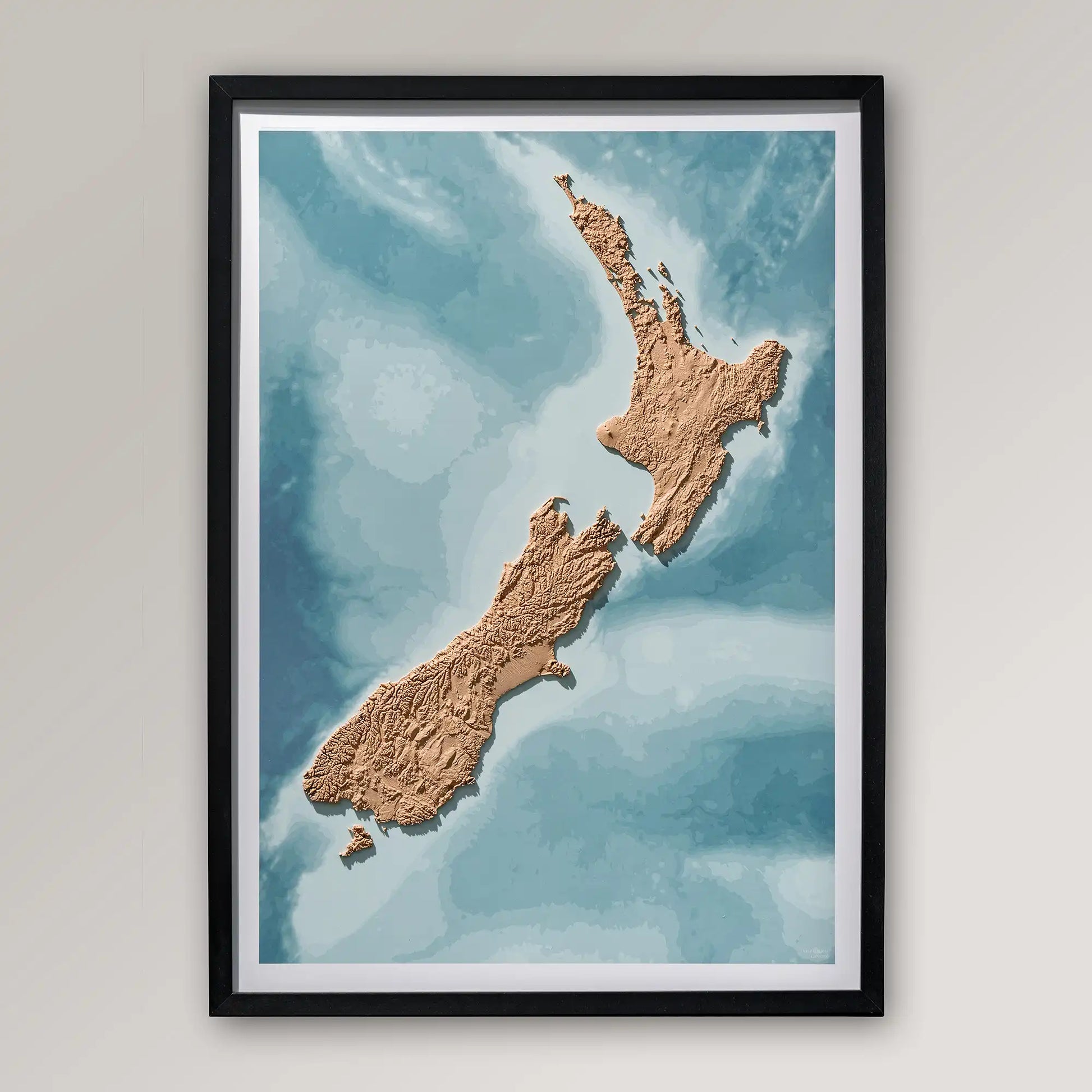 Framed 3D topographic map of New Zealand inside a black frame on a light grey wall – TerraFrames