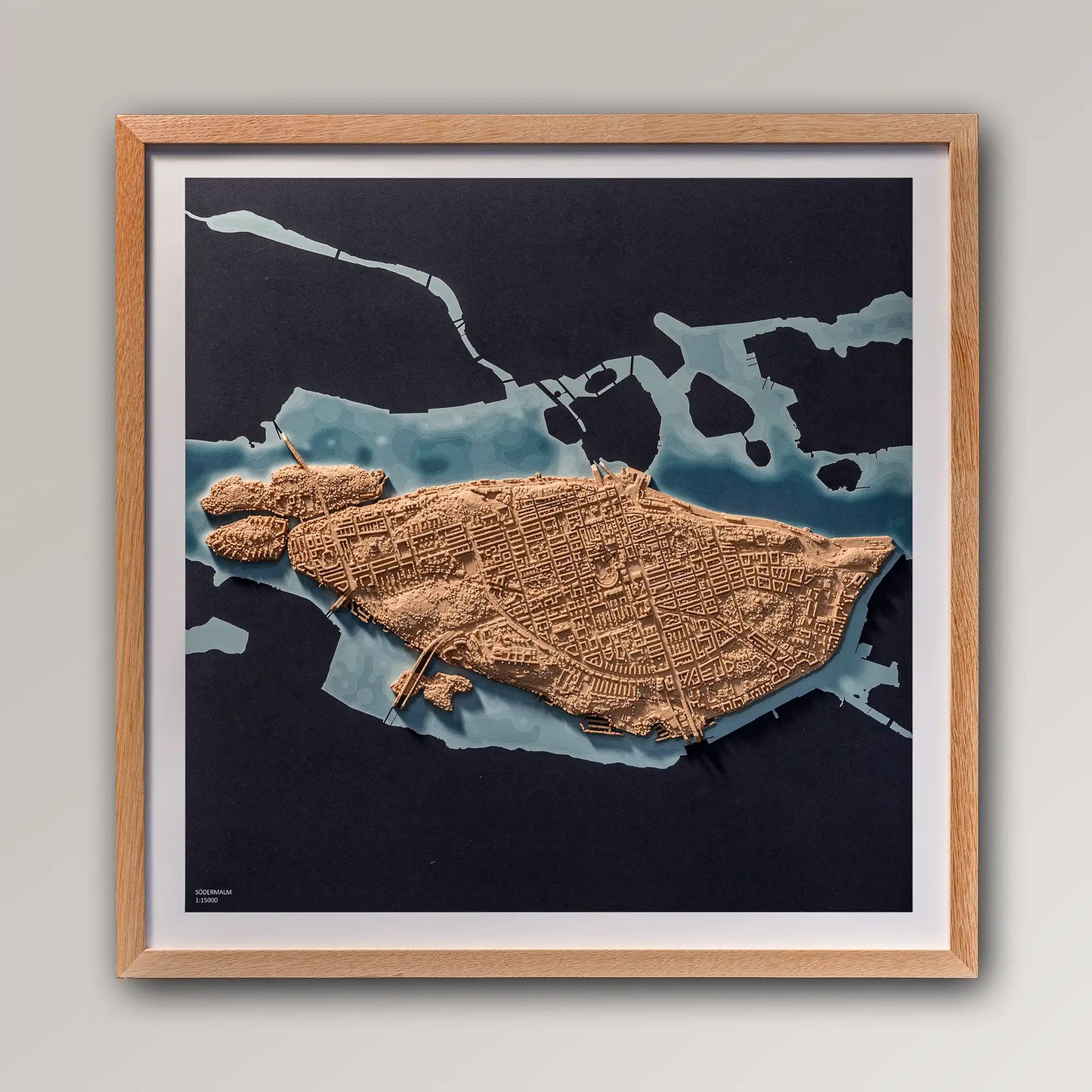Framed 3D topographic map of Södermalm, Stockholm, 40x40cm art board inside an oak frame on a light grey wall – TerraFrames